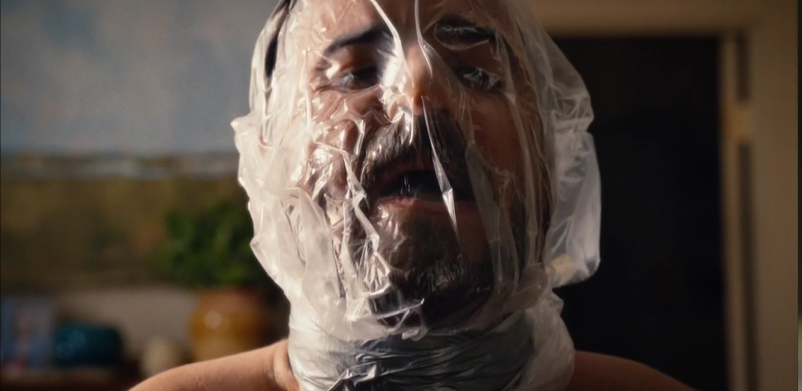 A man with a plastic bag wrapped around his head, inhaling.