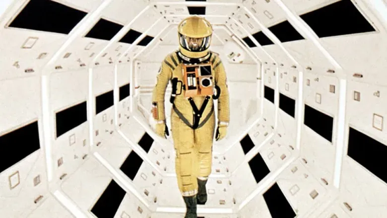 A person dressed in yellow space suit walking in a vast, futuristic space station and illuminated pathways